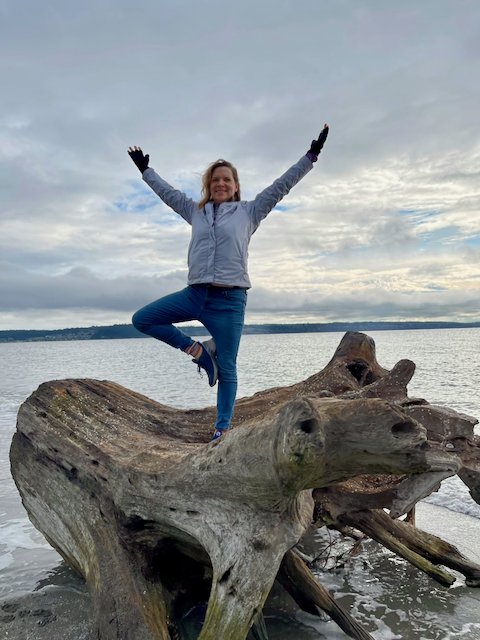 Kate Conway Larson in tree pose on a driftwood log at the edge of Puget Sound